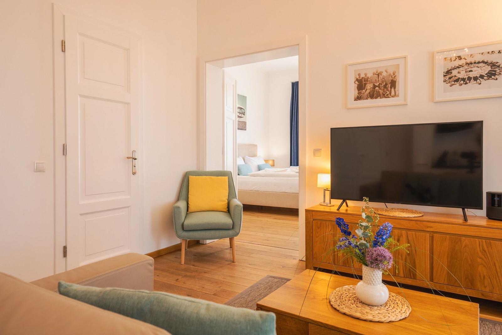 Wohnzimmer mit Fernseher, Sessel und Blick in Schlafzimmer
