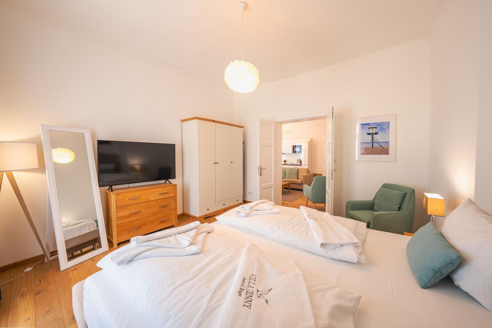 Schlafzimmer mit Bett, Fernseher und Kleiderschrank. Tür führt in Wohnbereich.