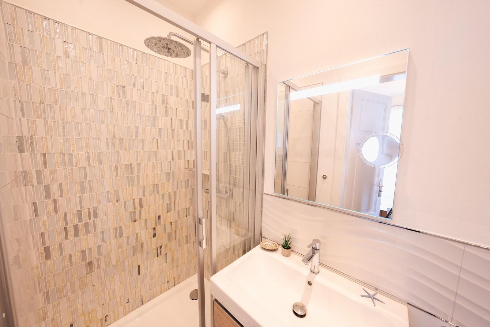 Badezimmer mit Dusche, Waschbecken und Spiegel