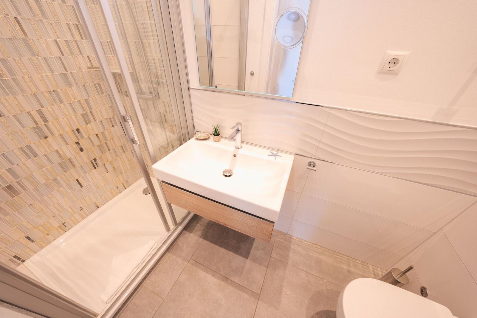 Badezimmer mit Dusche, Waschbecken und Toilette. Wand mit Mosaik und Wellenfliesen.