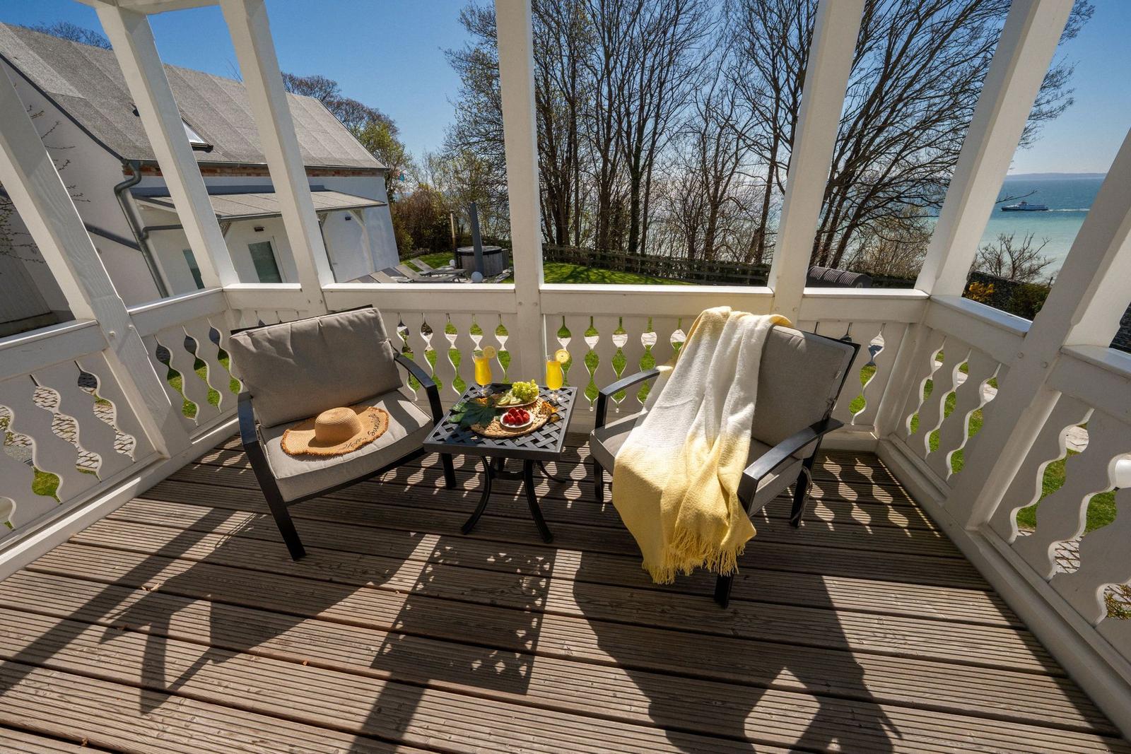 Terrasse mit zwei Stühlen und Tisch. Blick auf See und Bäume.