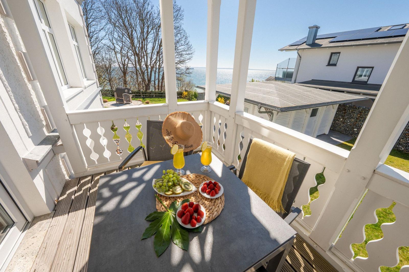 Terrasse mit Tisch, Stühlen und Obstansicht auf Wasser und Garten.