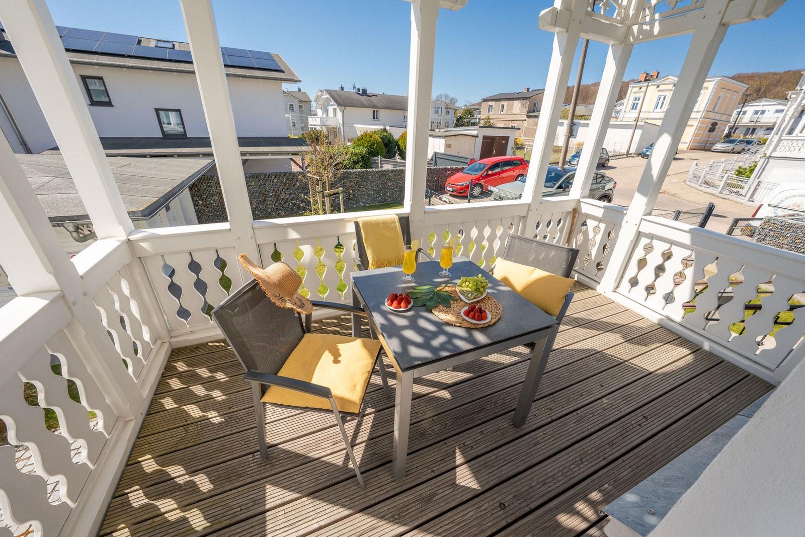 Terrasse mit Tisch, Stühlen und Obst. Weiße Brüstung und Blick auf die Straße.