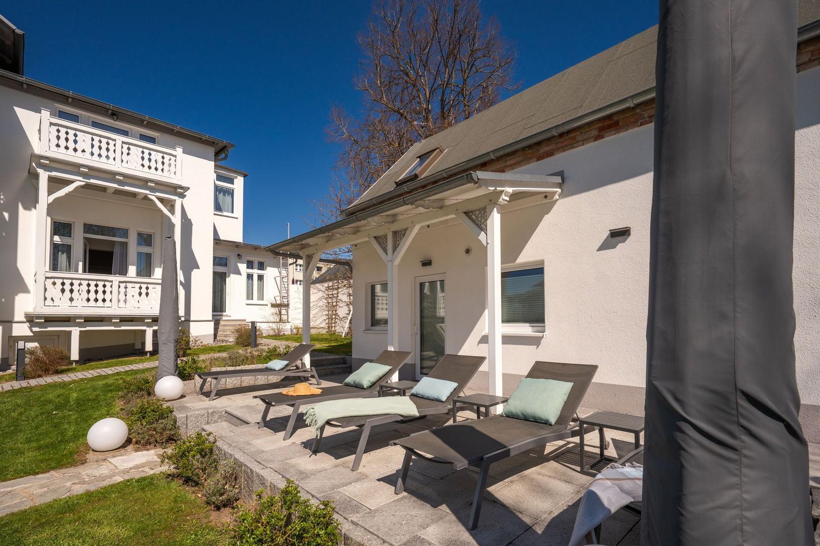 Terrasse mit Liegen und Garten. Hinterhof mit weißen Häusern und blauem Himmel.