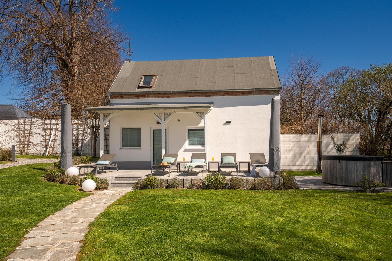 Wohnhaus mit Terrasse, Liegen und Whirlpool im Garten.