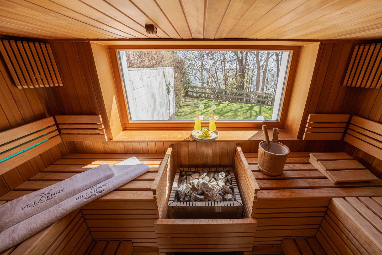 Holzsauna mit Blick auf Garten. Steine, Kissen und Getränke bereit.