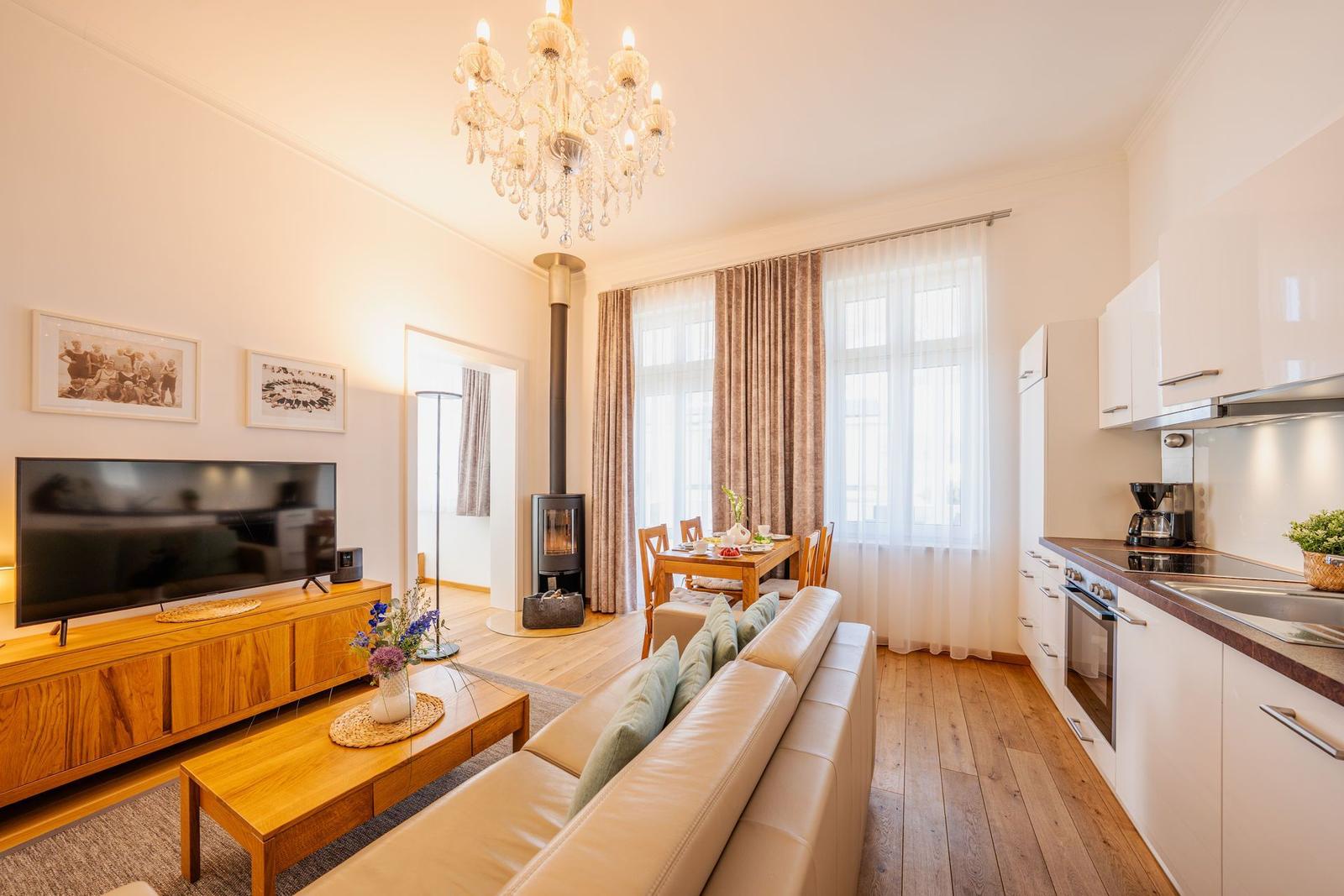 Wohnküche mit Sofa, TV, Esstisch und Kaminofen. Holzboden und weiße Küchenzeile.