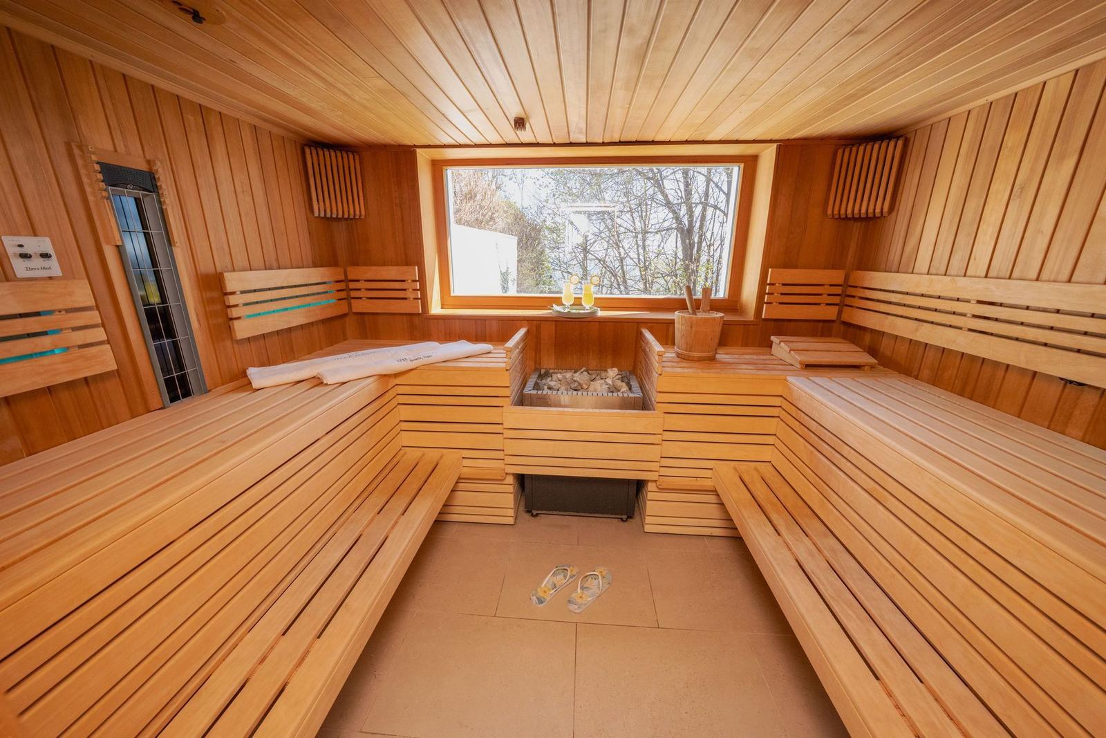 Sauna mit Holzbanken, Steinofen und Fensterblick auf Bäume