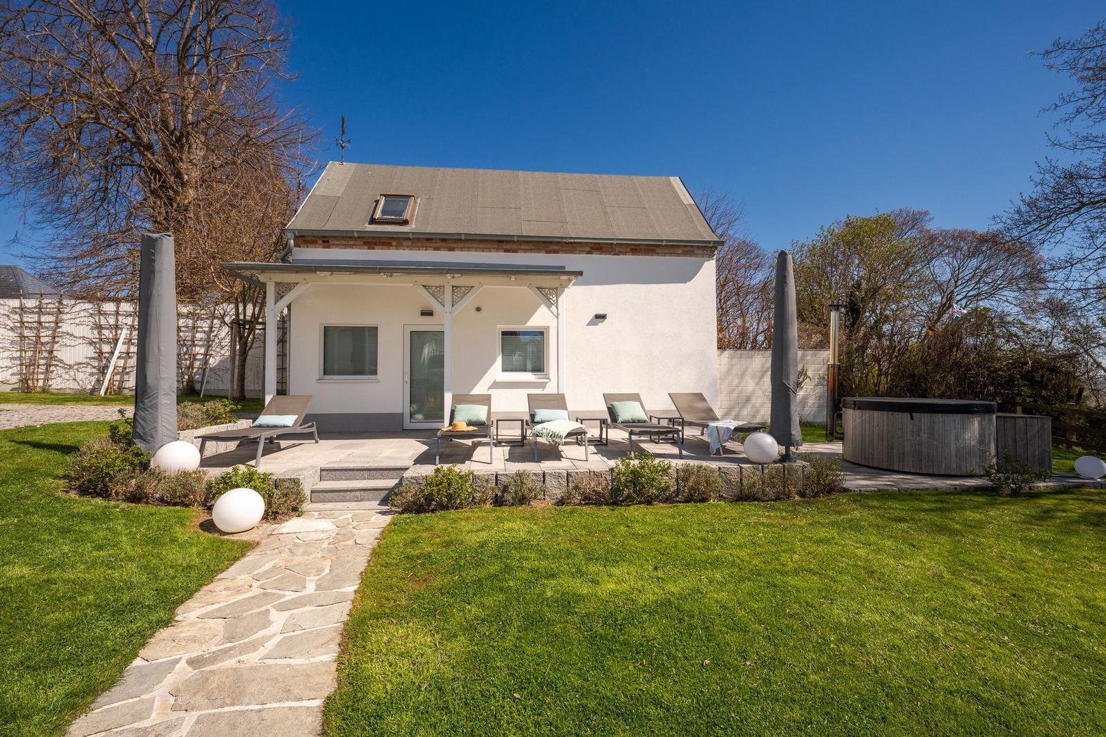 Haus mit Terrasse, Liegen und Whirlpool im Garten. Steinerne Wegführung durch Rasen.