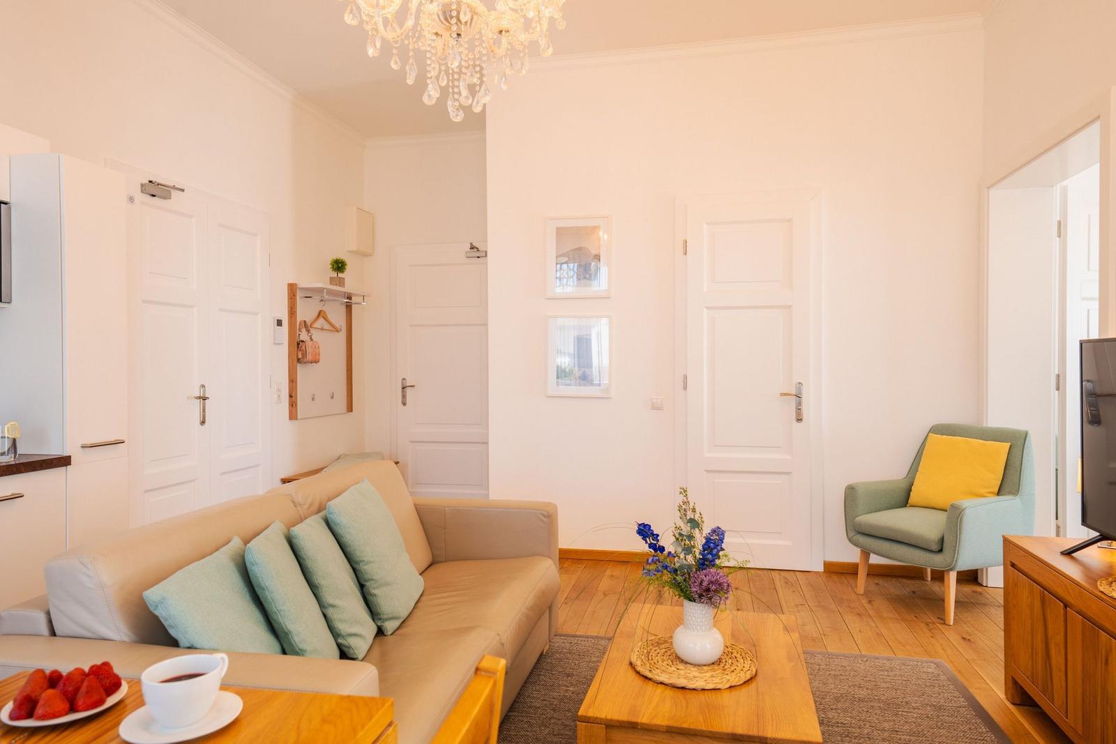 Wohnzimmer mit Sofa, Sessel, Couchtisch und Kronleuchter.
