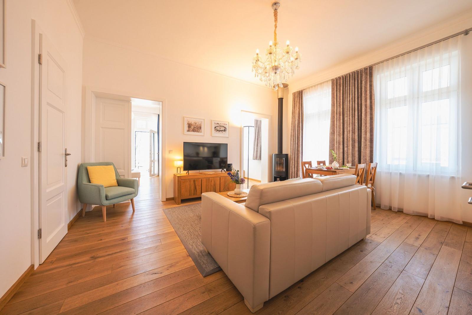 Wohnzimmer mit Sofa, Fernseher und Esstisch. Holzboden und große Fenster.