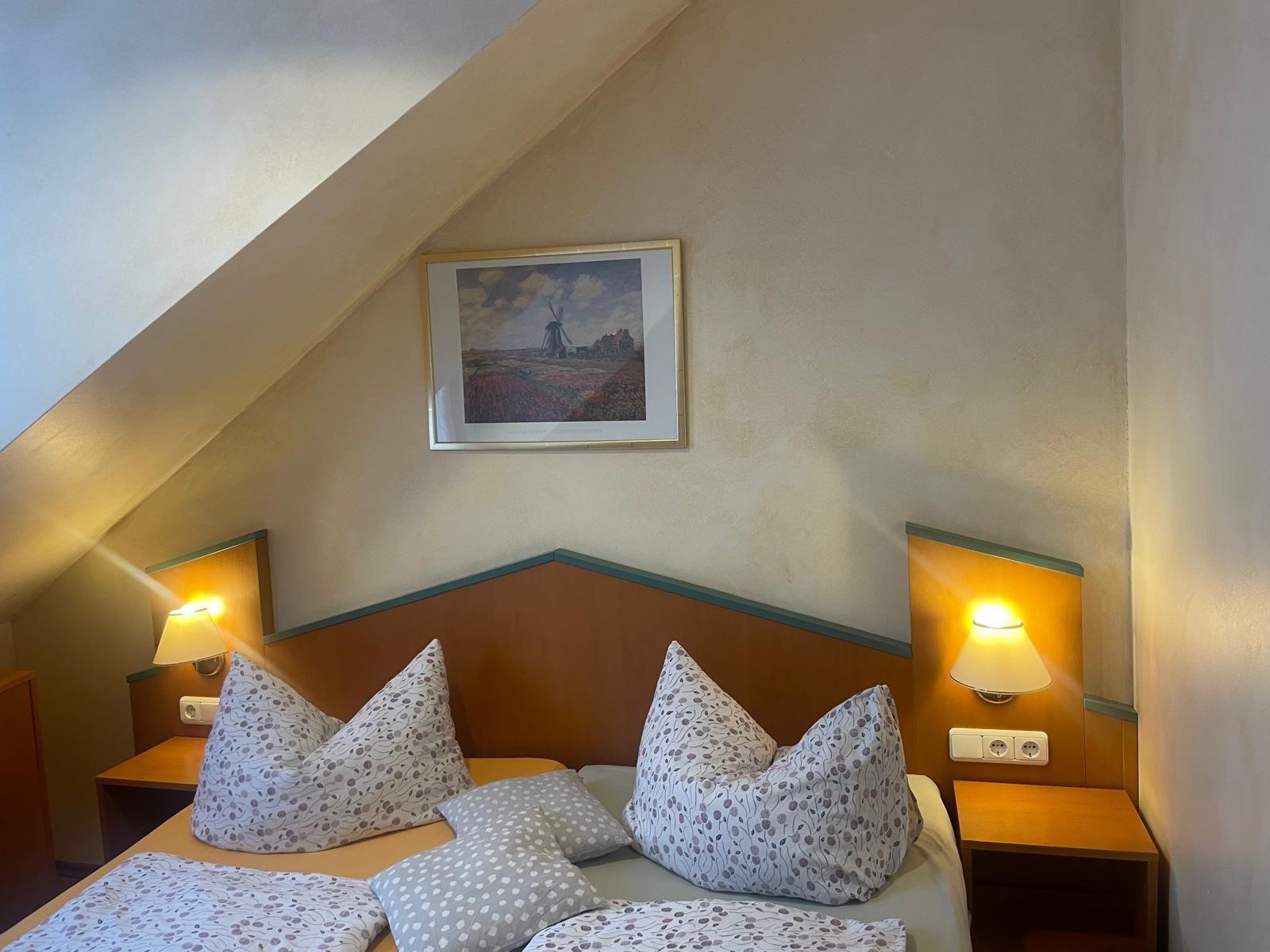 Schlafzimmer mit Dachschräge, Bett mit Kissen und zwei Nachttischen mit Lampen.
