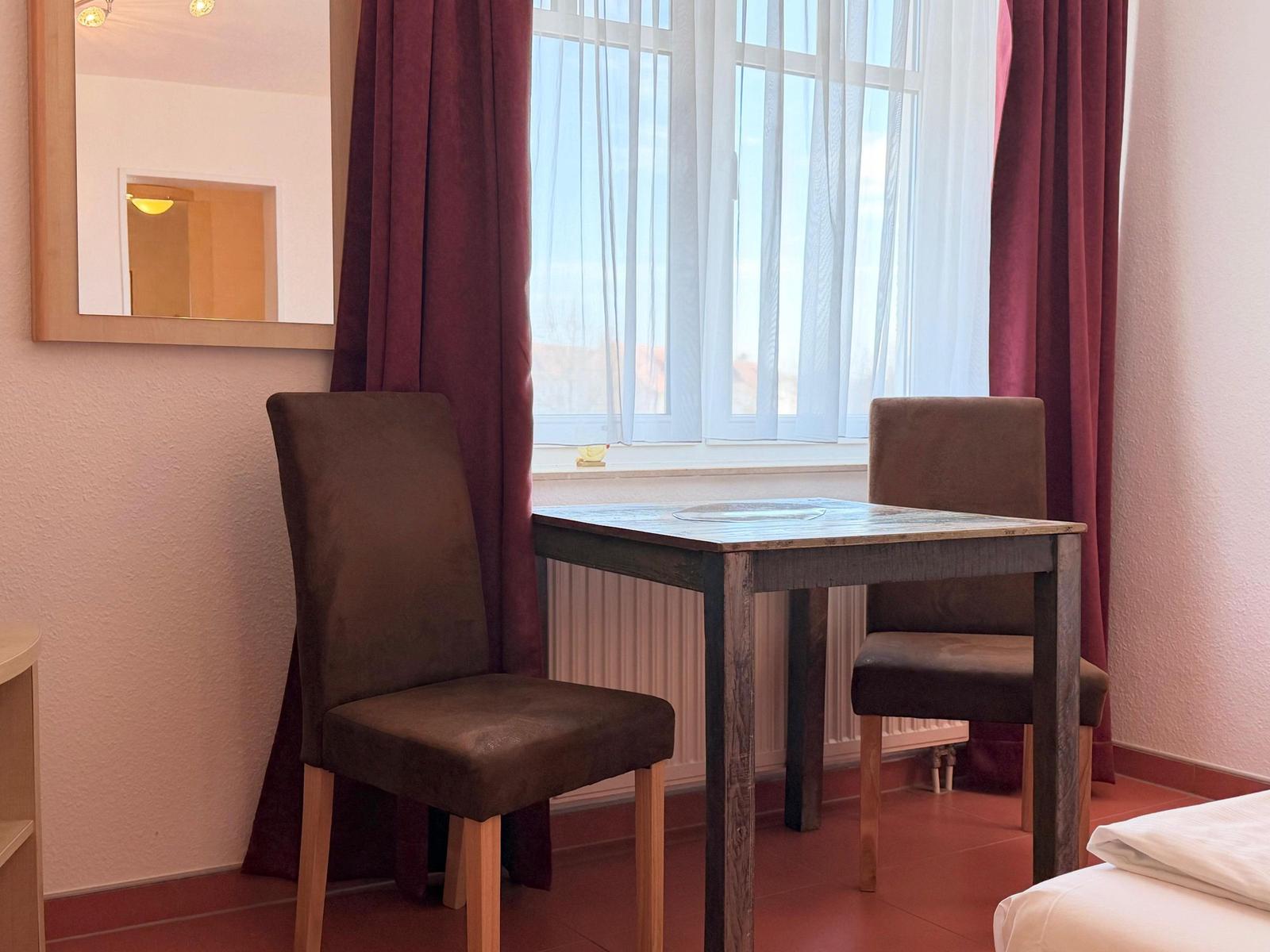 Ein Tisch mit zwei Stühlen vor einem Fenster mit Vorhängen.