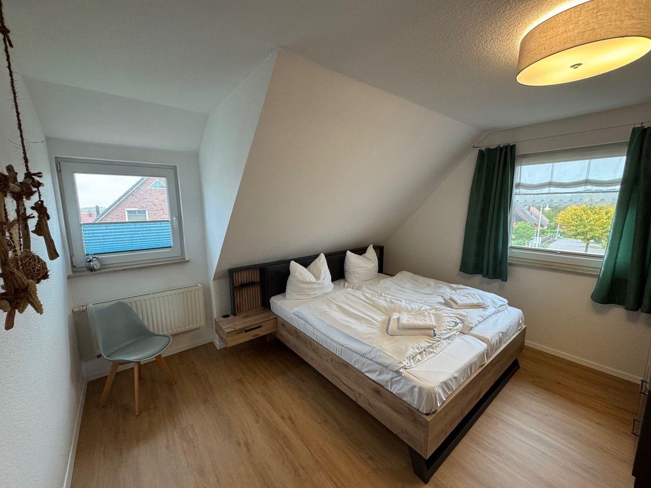 Schlafzimmer mit Doppelbett, zwei Fenstern und Holzboden.