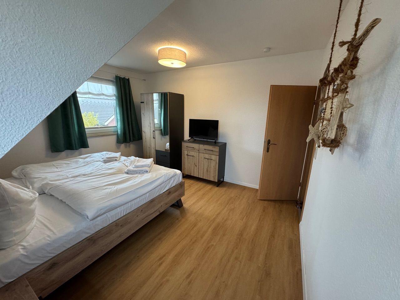 Schlafzimmer mit Bett, Fernseher und Holzboden unter Dachschräge
