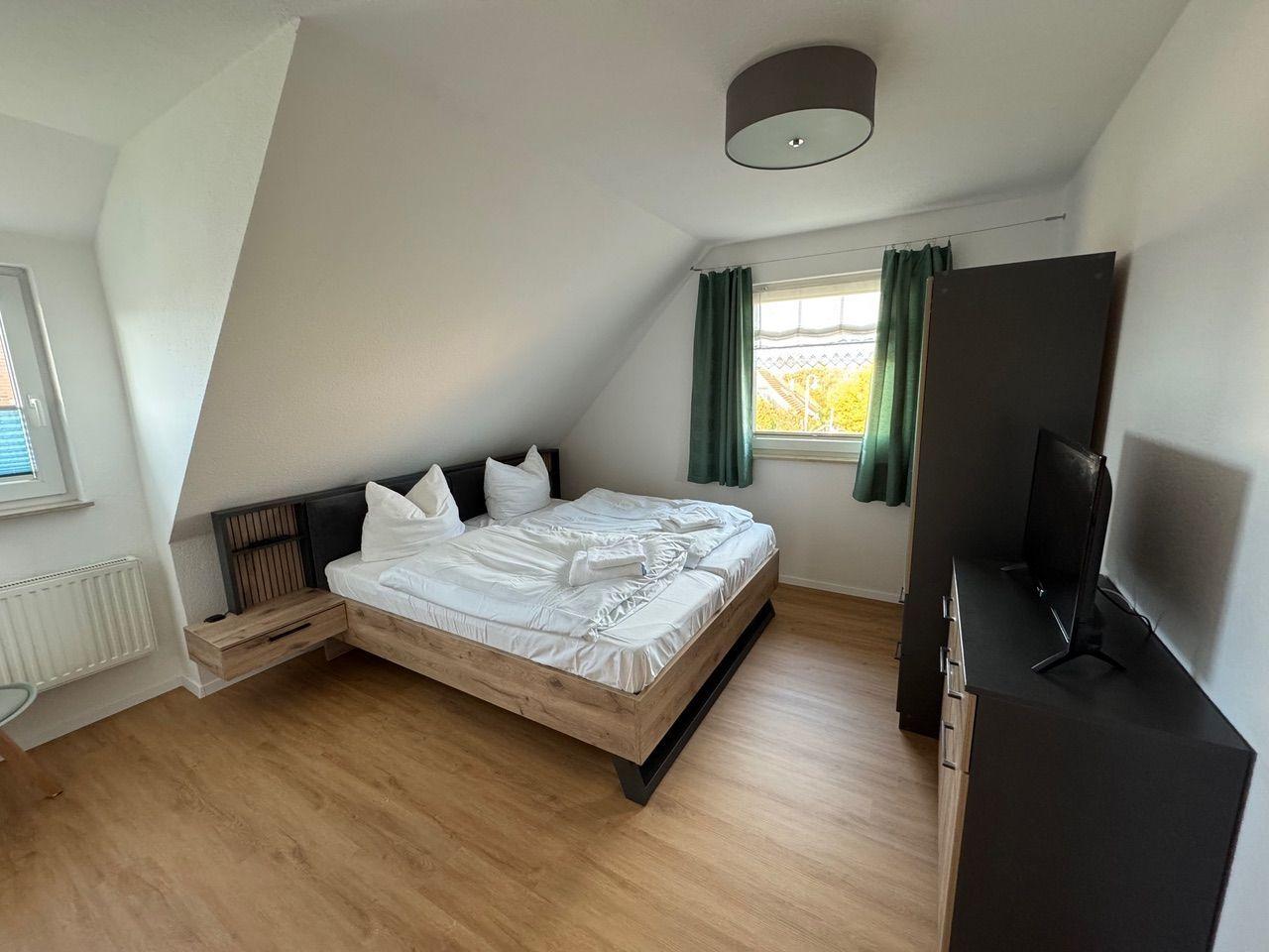 Schlafzimmer mit Doppelbett, Fenster, Kleiderschrank und TV.