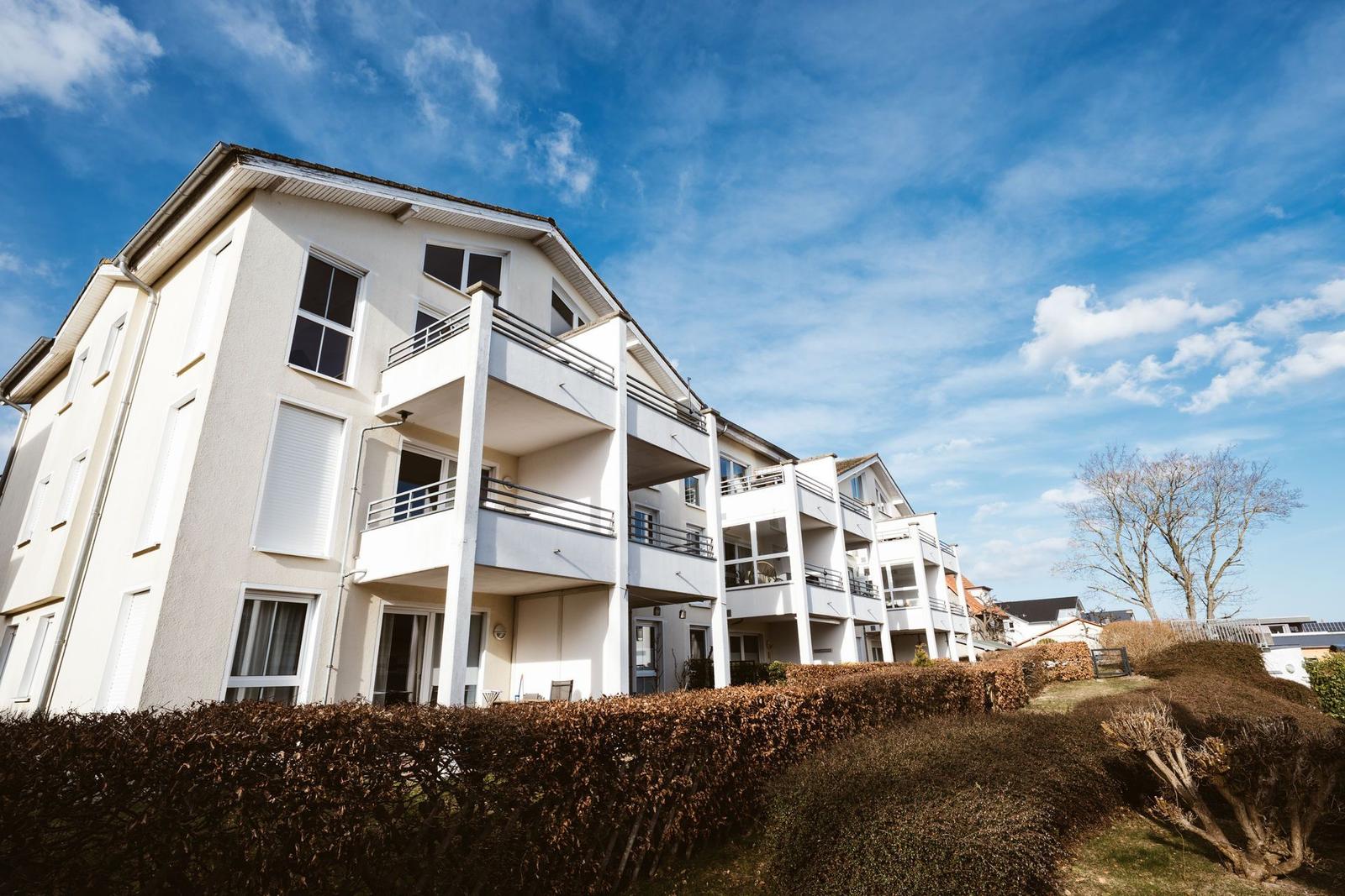 Wohnhaus mit Balkonen und begrünten Flächen unter blauem Himmel.