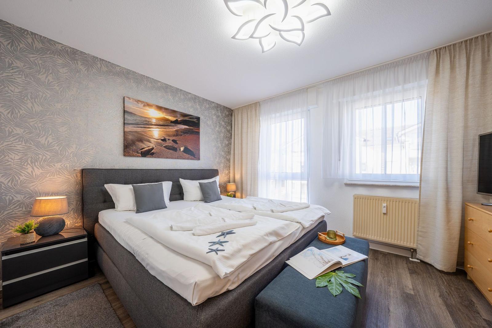 Schlafzimmer mit Doppelbett, Fenster, Nachttisch und Wandbild.