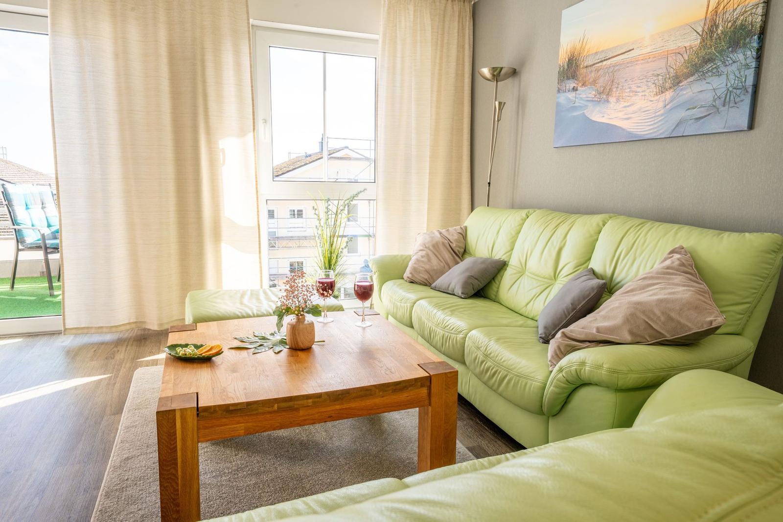 Ein Wohnzimmer mit grünem Sofa, Holztisch und Blick auf Balkon.