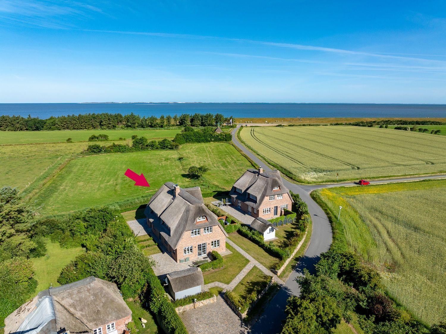 Dorfhaus mit Strohdach, umgeben von Feldern und Meer.