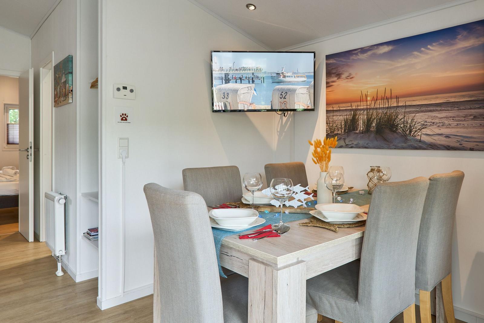 Esszimmer mit Tisch, Stühlen und Wandbild. Fernseher und Tür zur Schlafzimmer.
