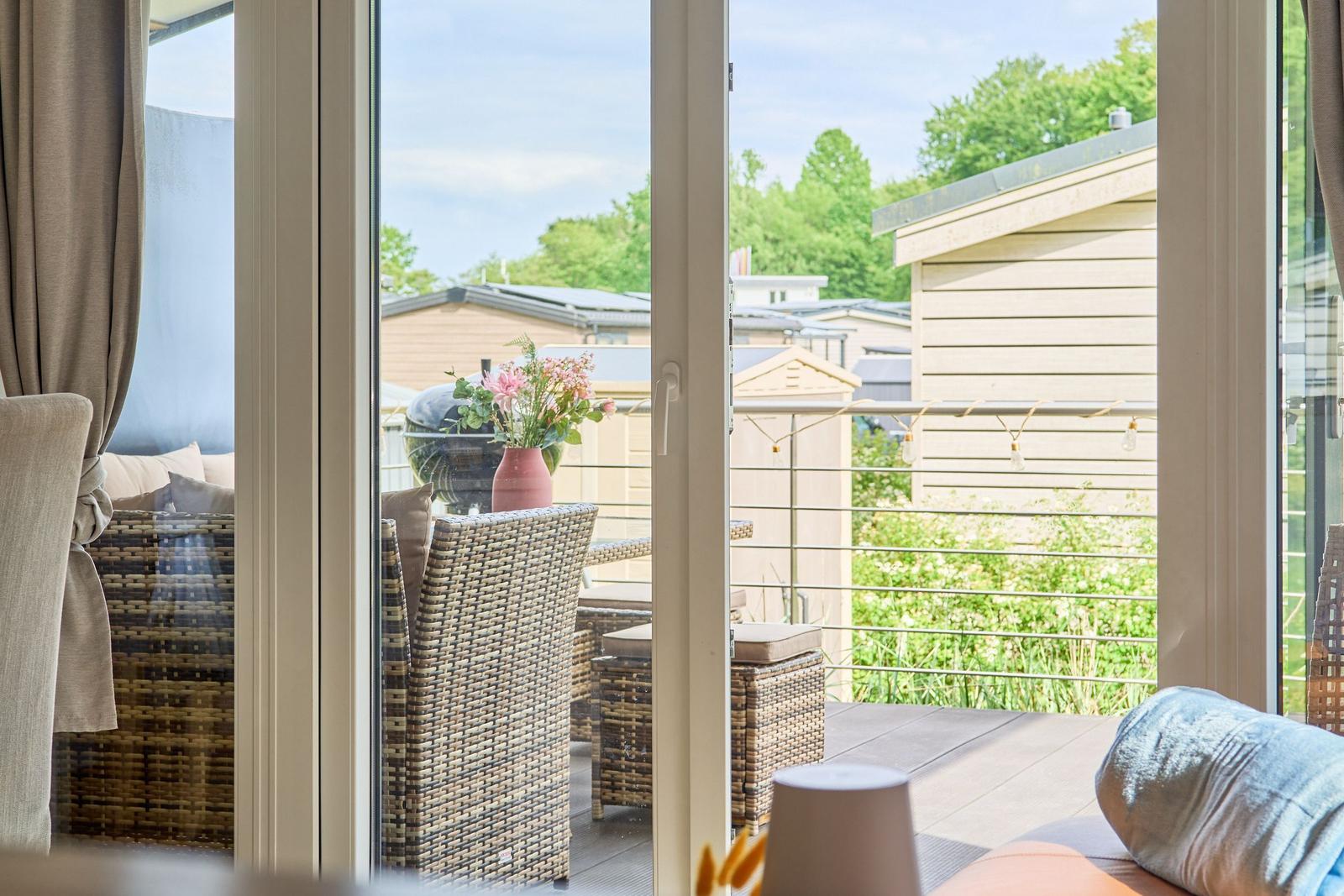 Terrasse mit Wickermöbeln und Blumen. Blick auf Garten und Nachbarhäuser.
