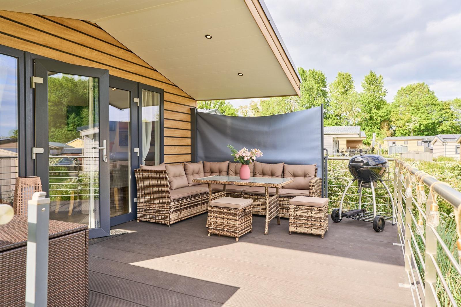 Terrasse mit Sitzgruppe, Grill und Sonnenschutz vor modernem Haus.