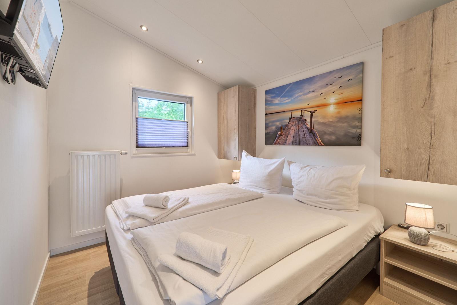 Schlafzimmer mit Doppelbett, Fenster, Nachttisch und Wandbild.