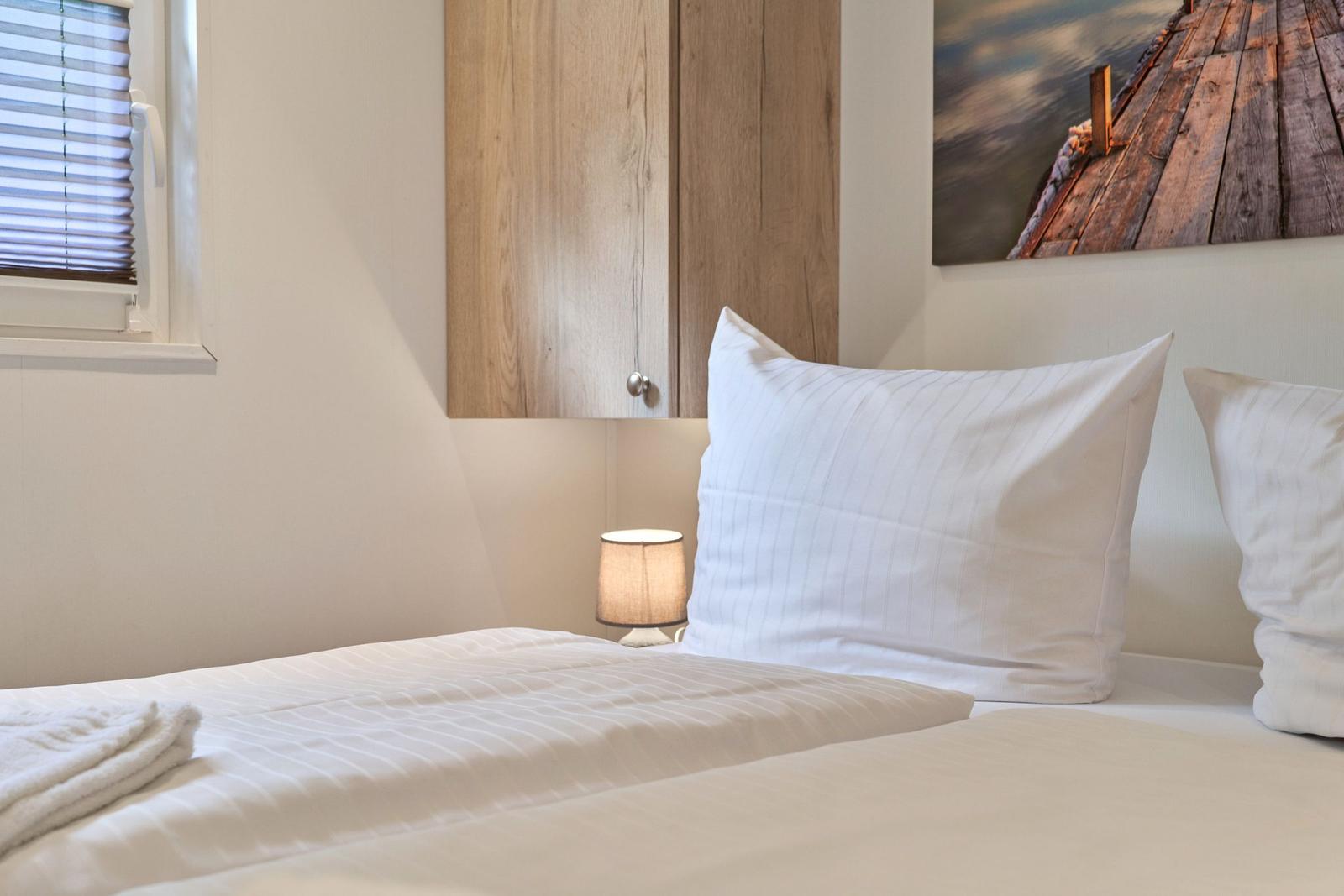 Schlafzimmer mit Bett, Kissen, Nachttischlampe und Holzschrank an der Wand.