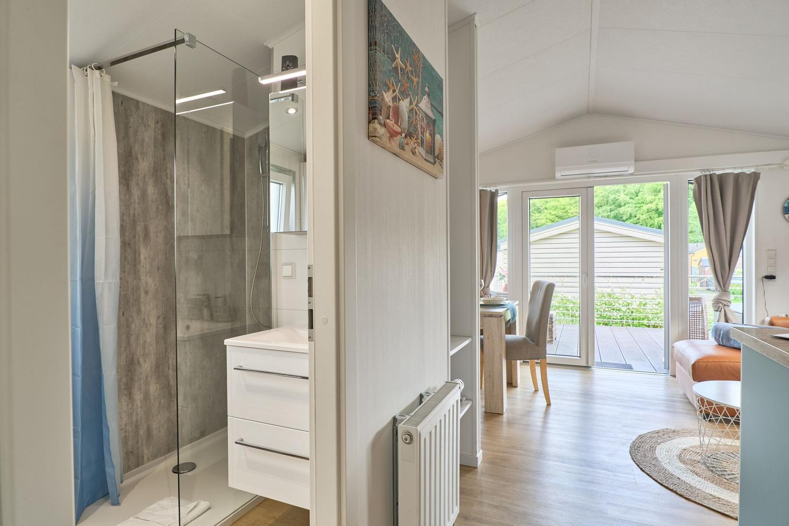 Badezimmer mit Dusche und Waschbecken. Wohnbereich mit Terrasse und Esstisch.