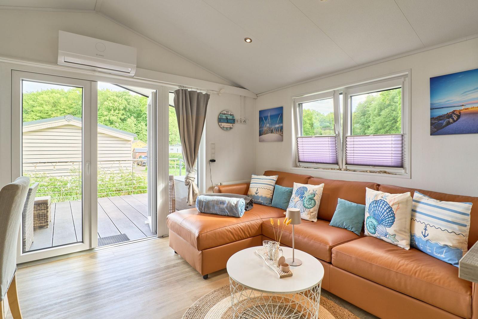 Ein Wohnzimmer mit braunem Sofa, runden Tisch und Blick auf eine Terrasse.