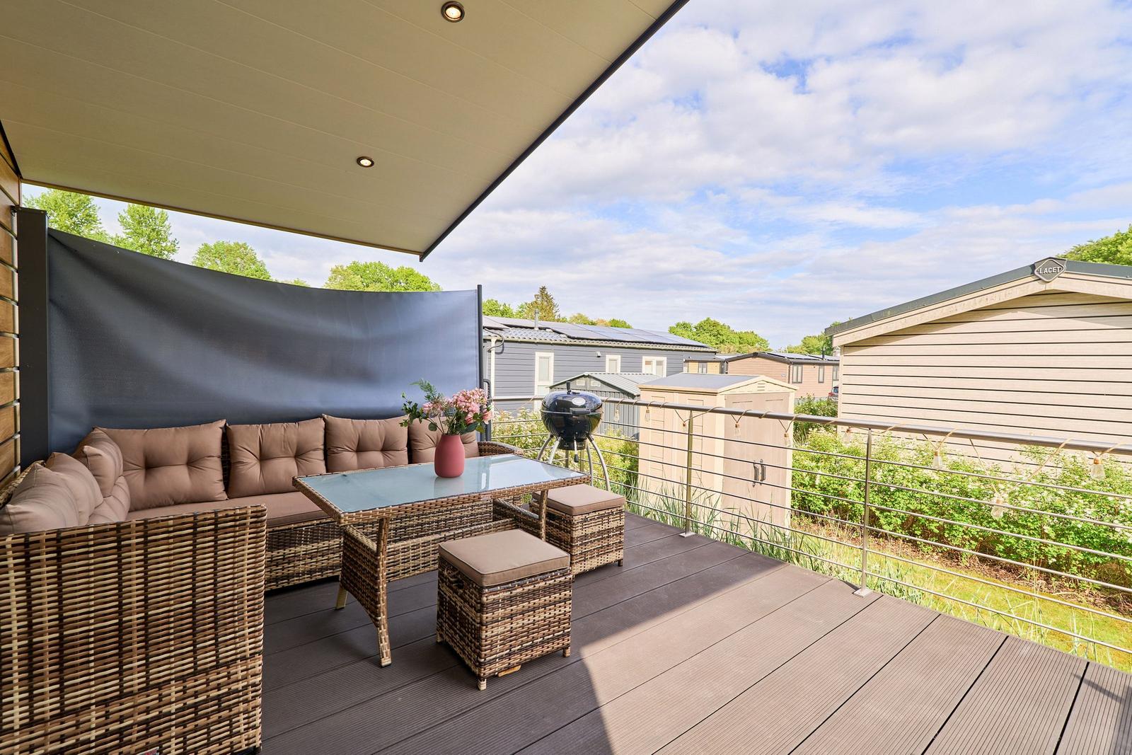 Terrasse mit Sitzgruppe, Tisch und Grill. Blick auf Wohnmobile und Grünflächen.
