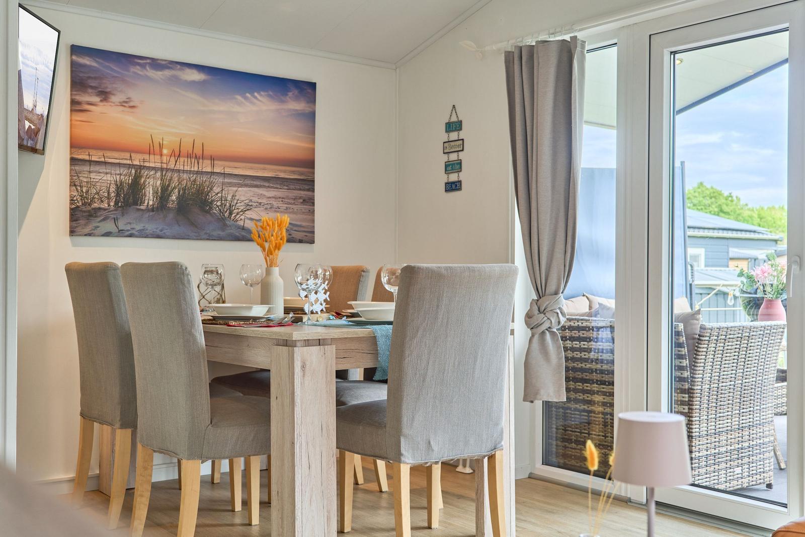 Esstisch mit Stühlen, Wandbild und Terrassentür mit Blick auf die Außenterrasse.