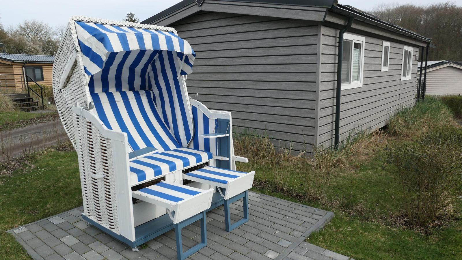 Ein Strandkorb mit blau-weißem Streifenmuster steht vor einem grauen Haus.