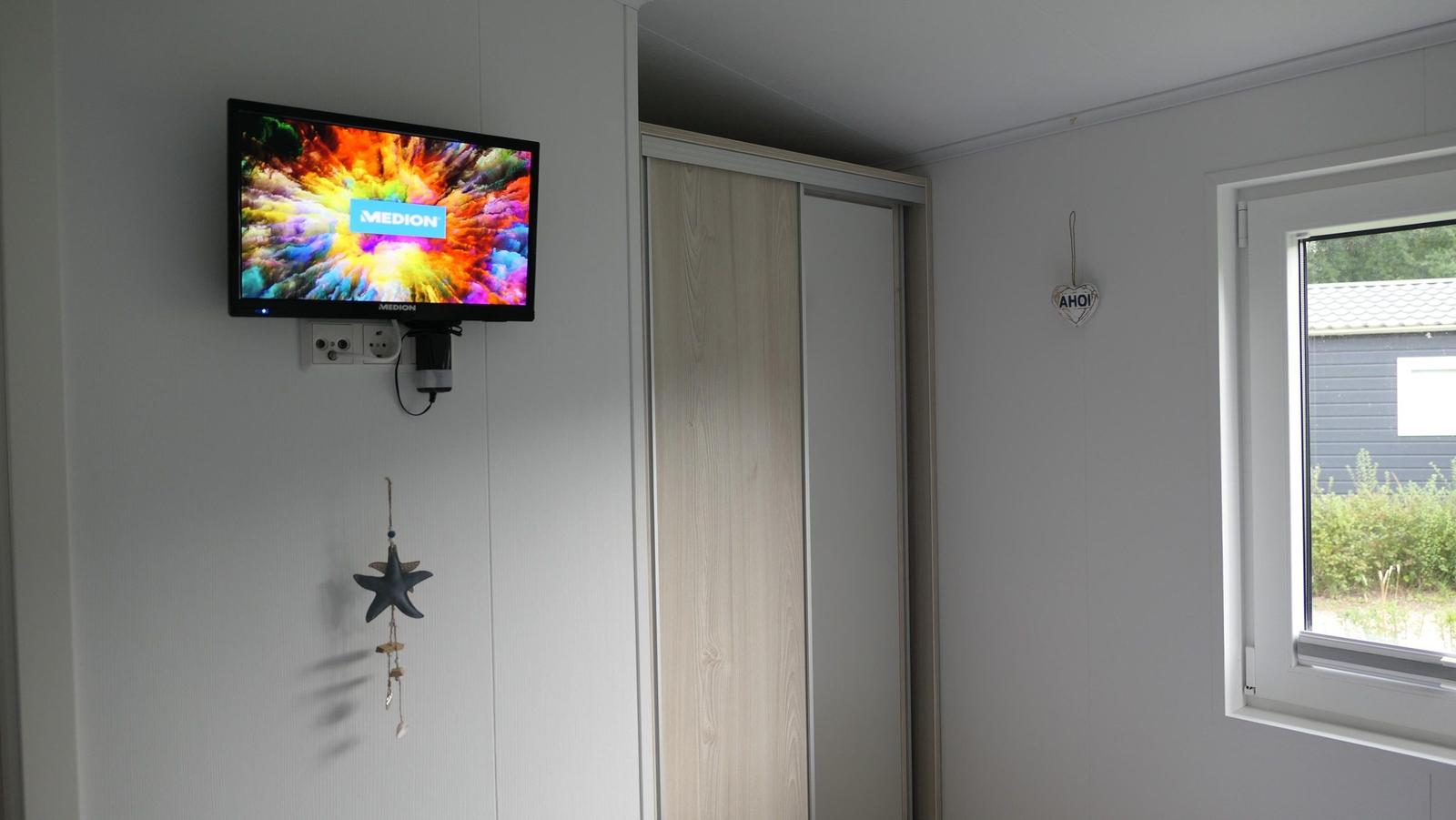 Wohnraum mit Wandfernseher, Schiebetür und Fenster mit Blick nach draußen.