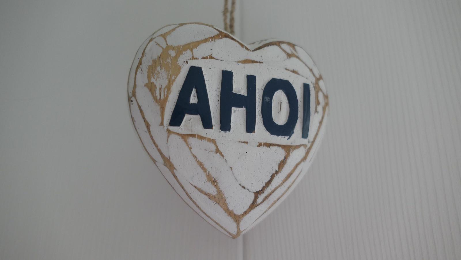 Herzformiges Schild mit der Aufschrift AHOI hängt an einer Wand.