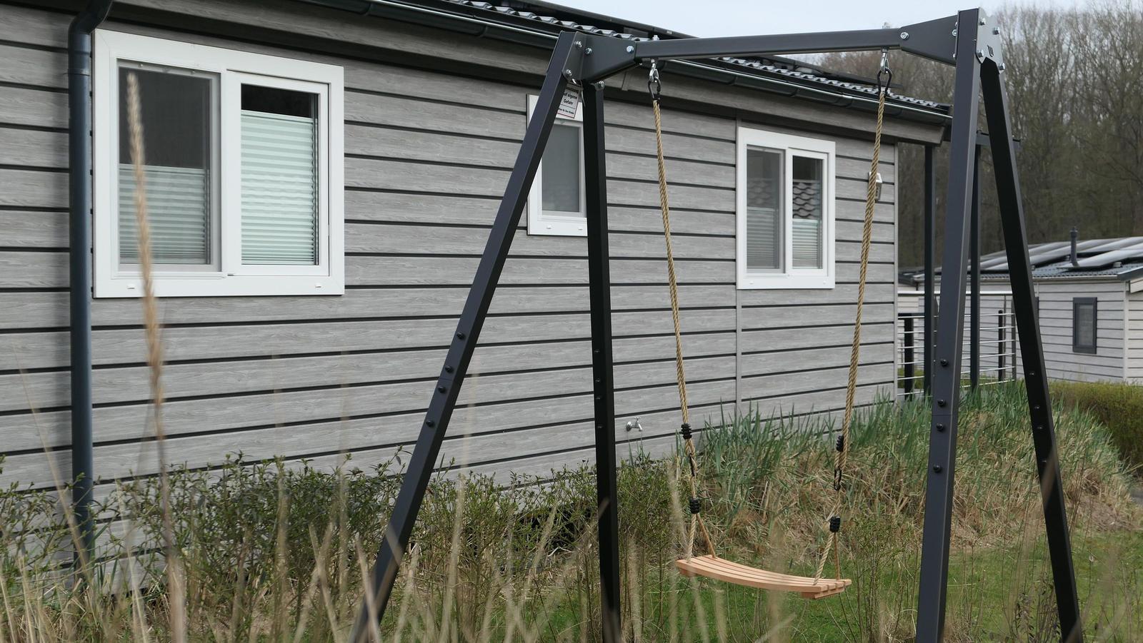 Schwingschaukel vor einem grauen Haus mit weißen Fenstern.