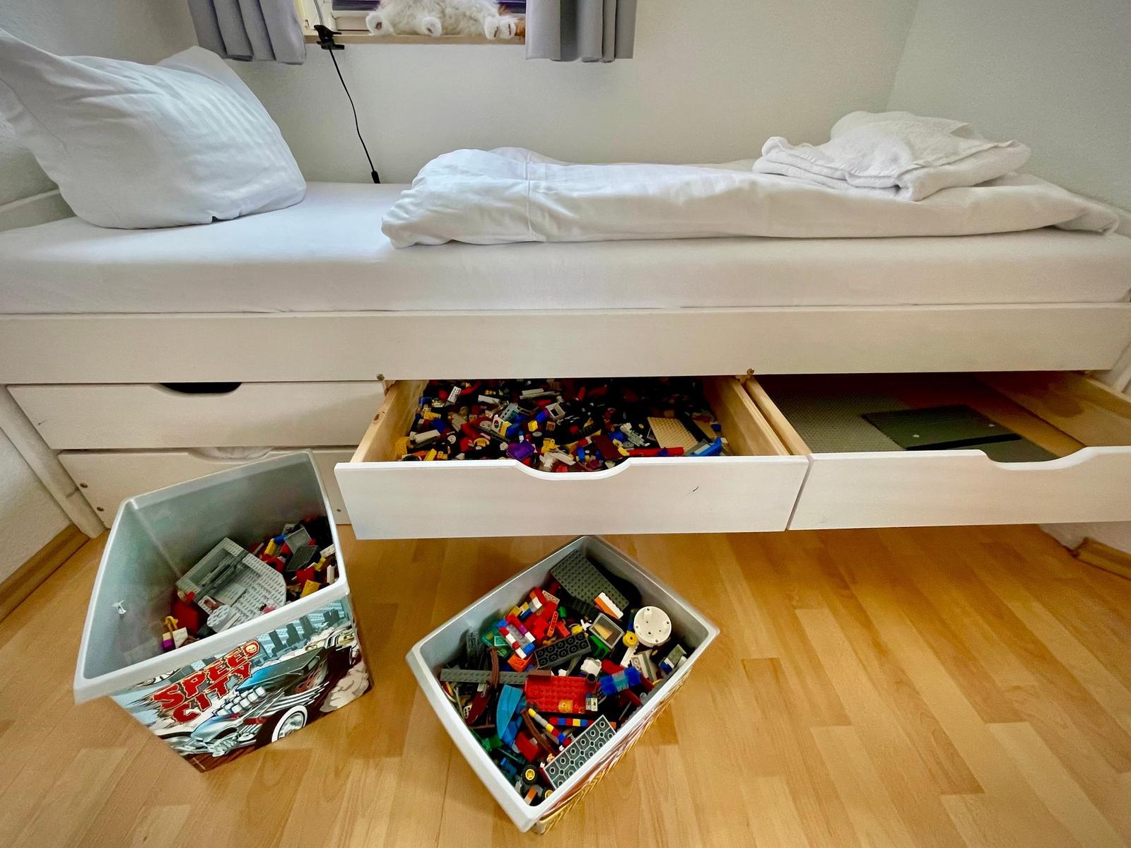 Schlafzimmer mit Bett, Schubladen und Spielzeugboxen mit Bausteinen.