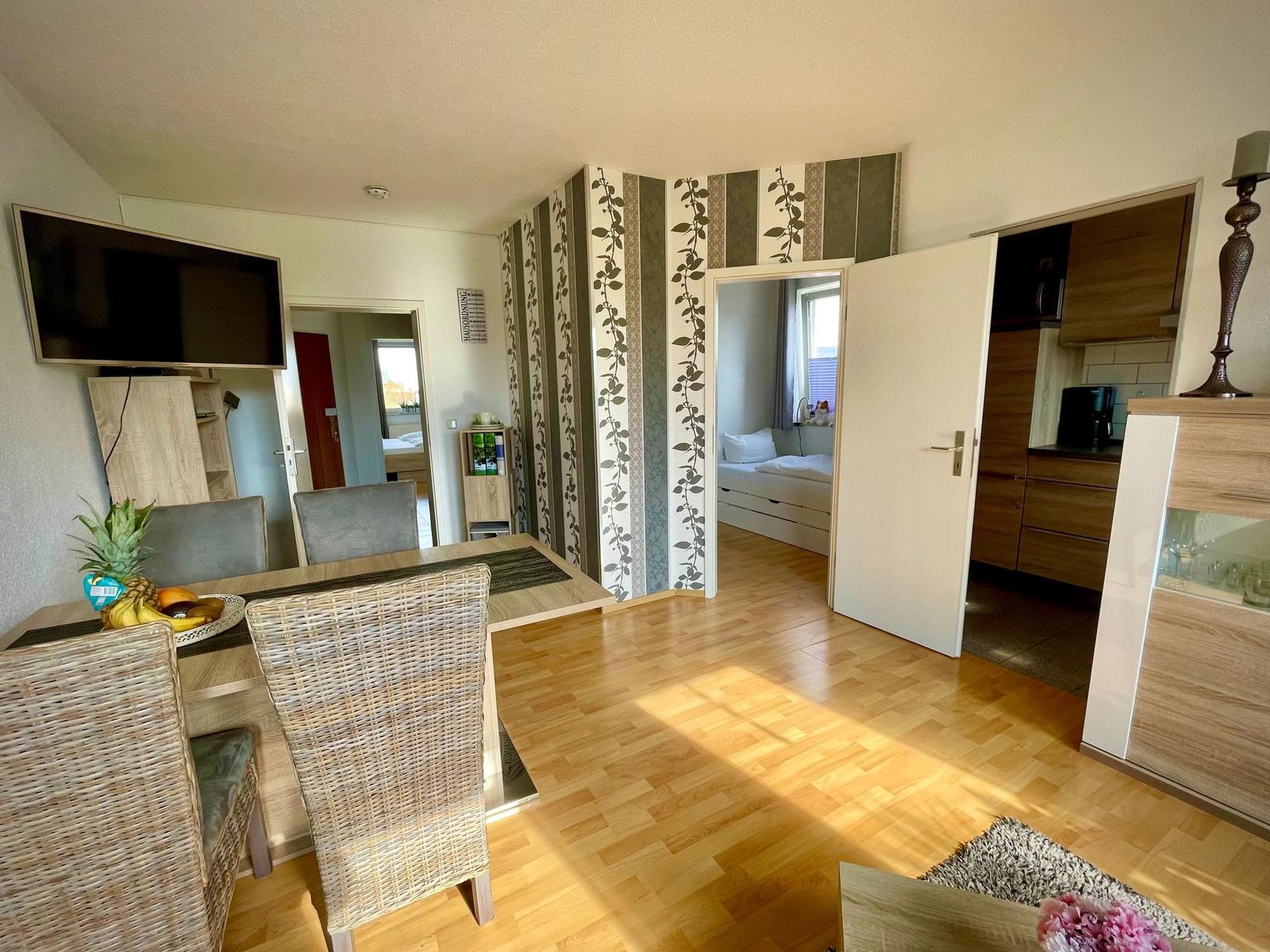 Wohnküche mit Esstisch, TV und Schlafzimmer im Hintergrund.