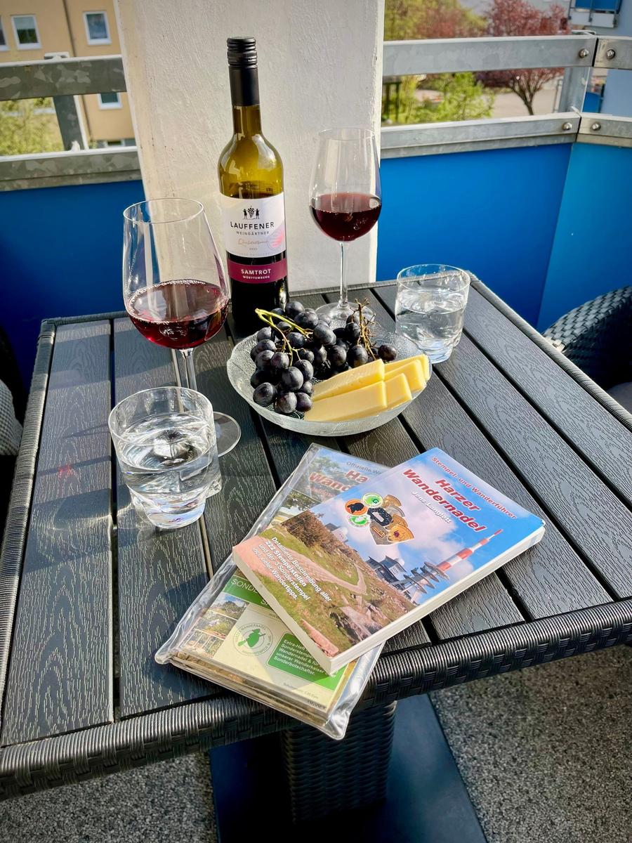 Auf der Terrasse steht ein Tisch mit Wein, Käse, Trauben und Wanderkarten.