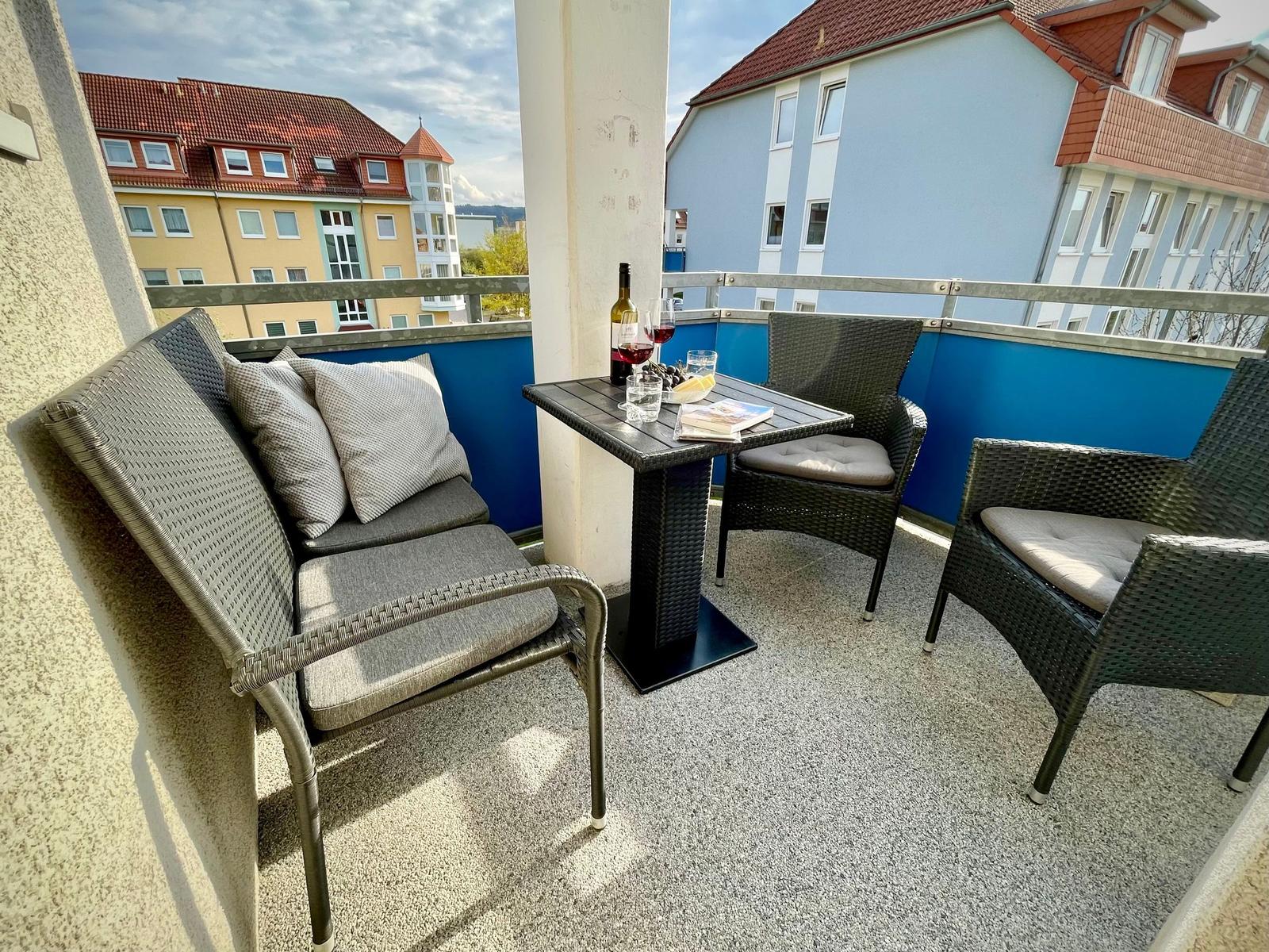 Terrasse mit Tisch und drei Stühlen, Blick auf Wohnhäuser.