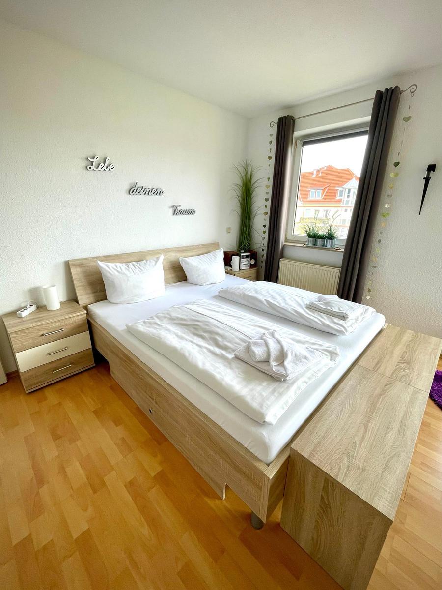 Schlafzimmer mit Doppelbett, Nachttisch und Fenster mit Blick auf Gebäude.