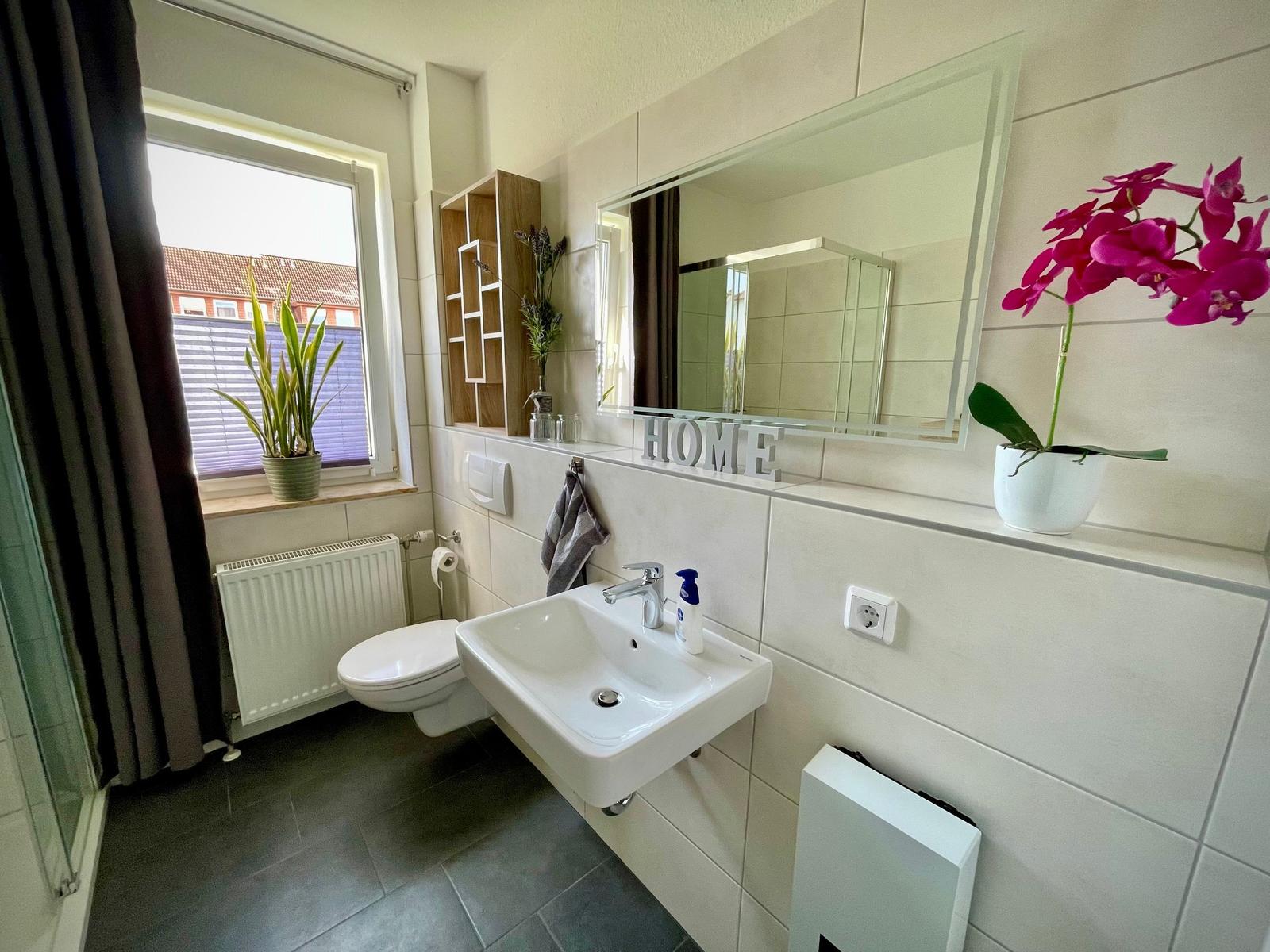 Badezimmer mit Waschbecken, Spiegel, Toilette und Pflanzen.