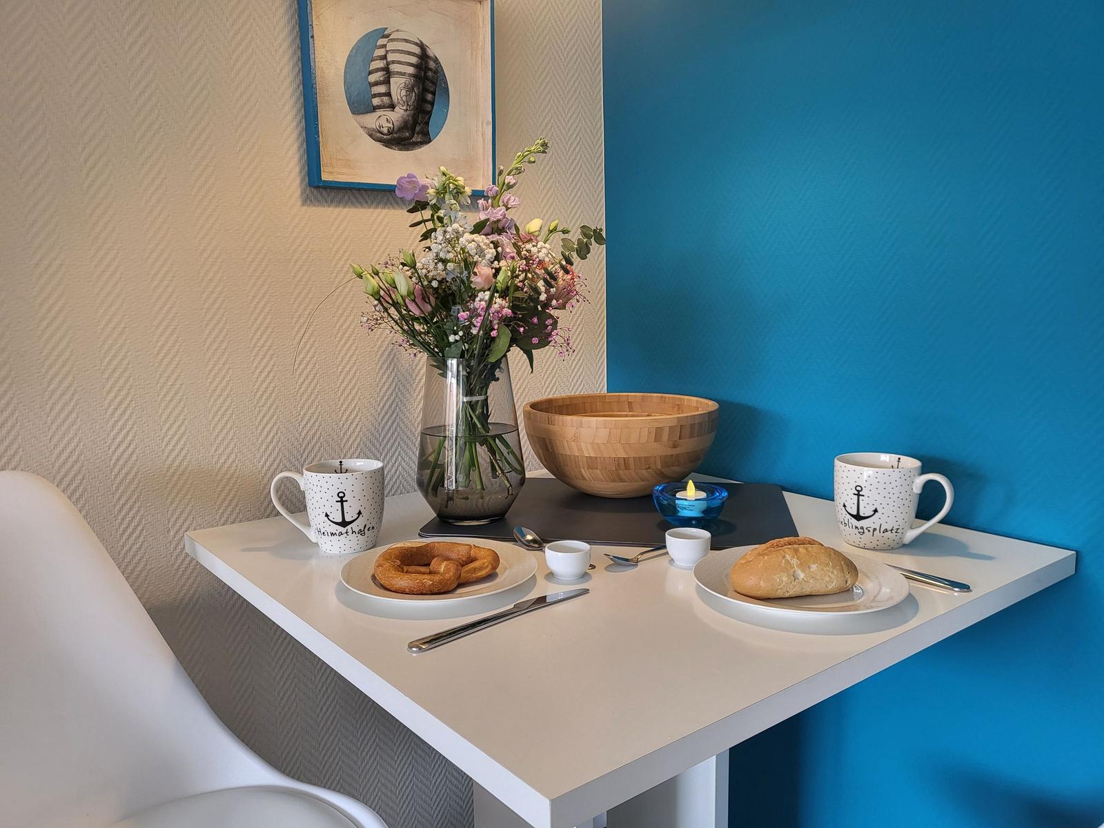 Table with coffee, bread, and flowers against blue wall