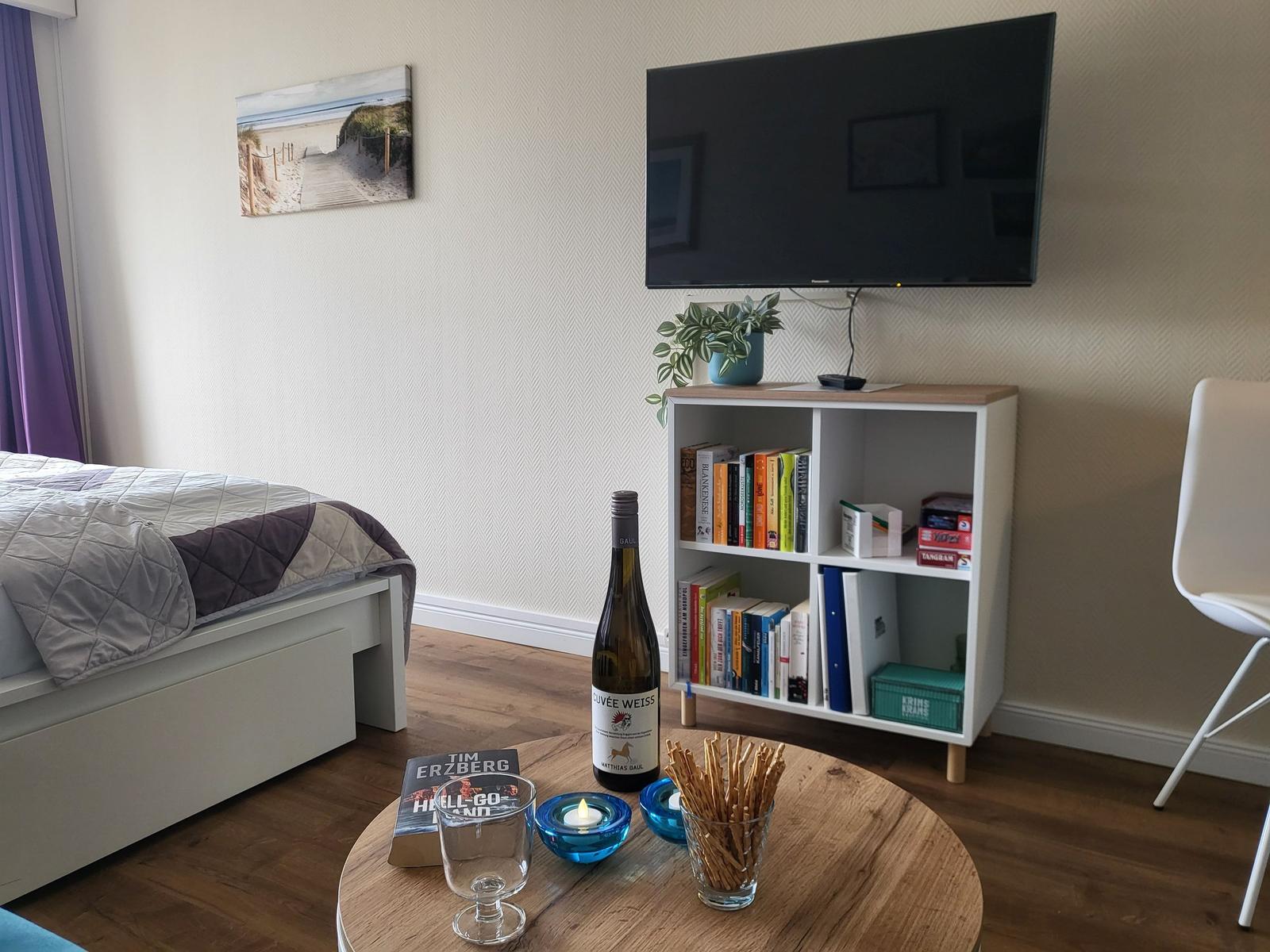 Bedroom with bed, TV, bookcase, and round table with drinks.