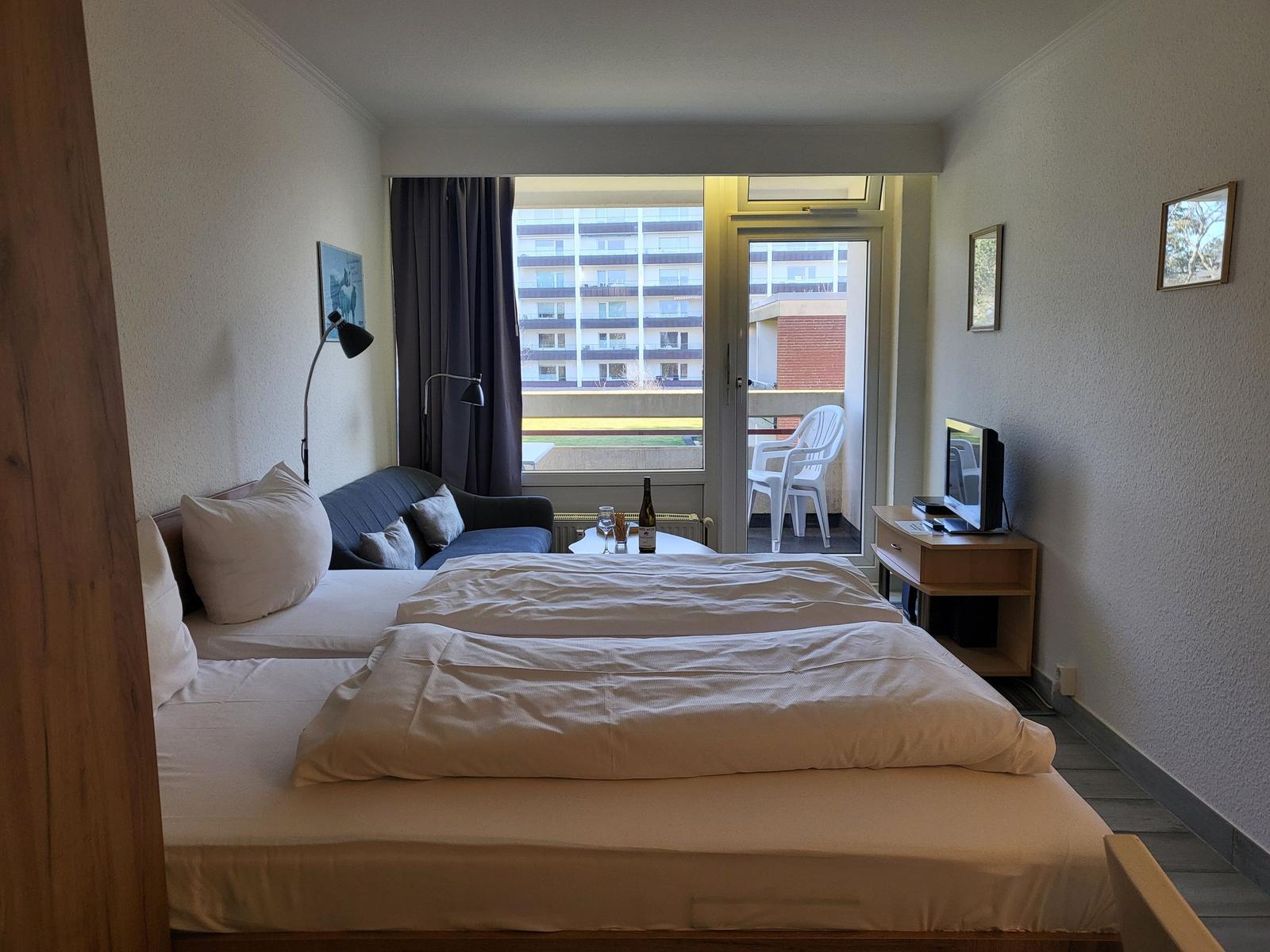 Zimmer mit Doppelbett, Sofa, TV und Balkon mit Stühlen.