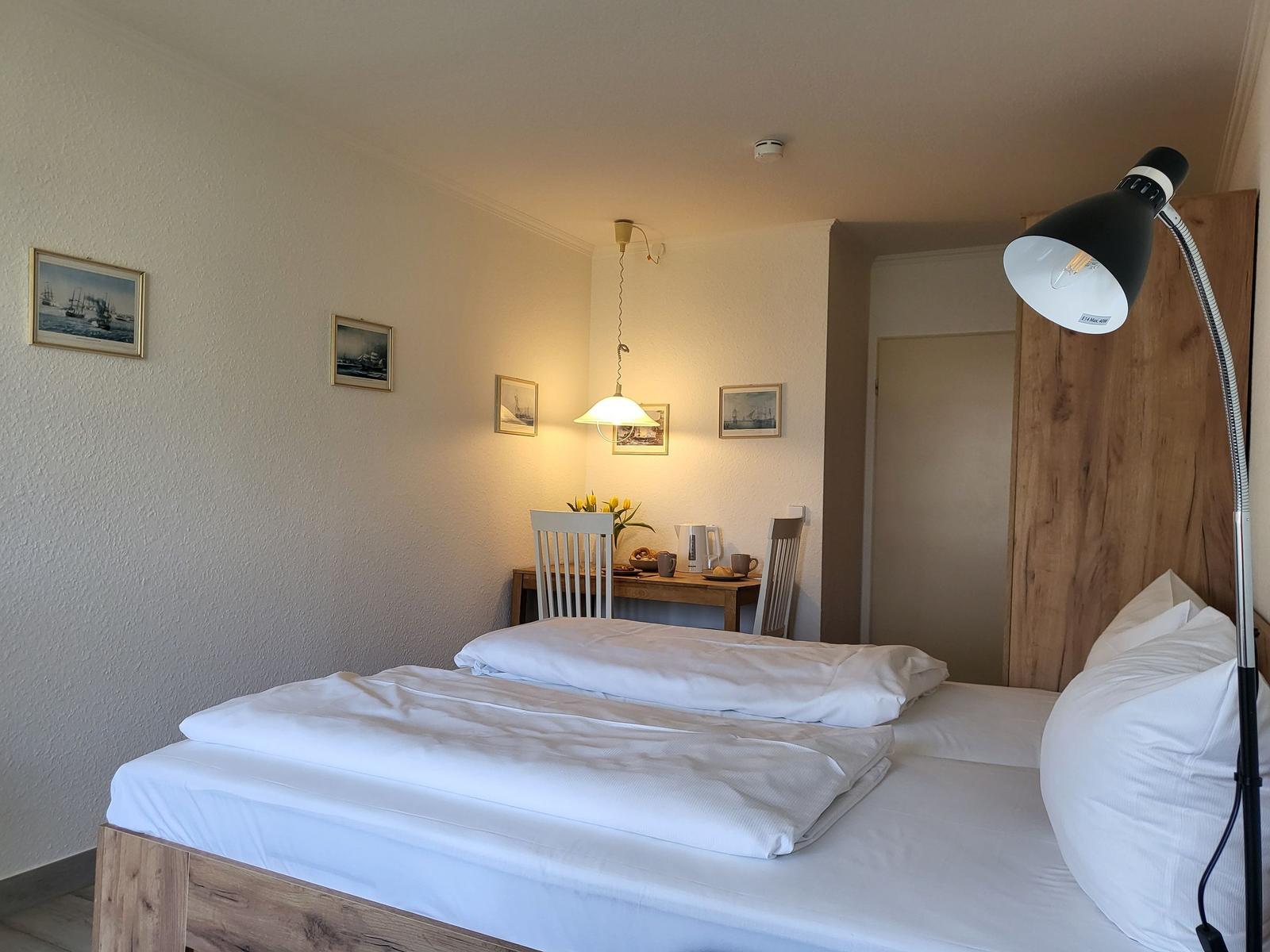 Schlafzimmer mit Bett, Tisch, Stühlen und Wandbildern.