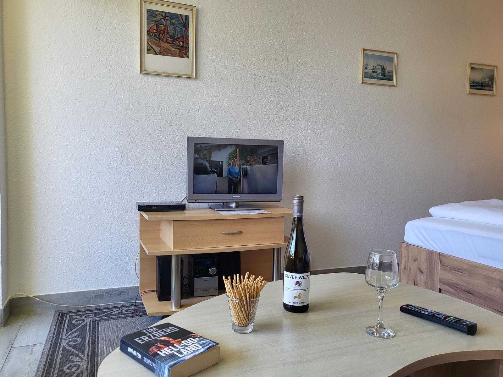 TV auf Holzkonsole, Flasche Wein, Gläser und Buch auf Tisch