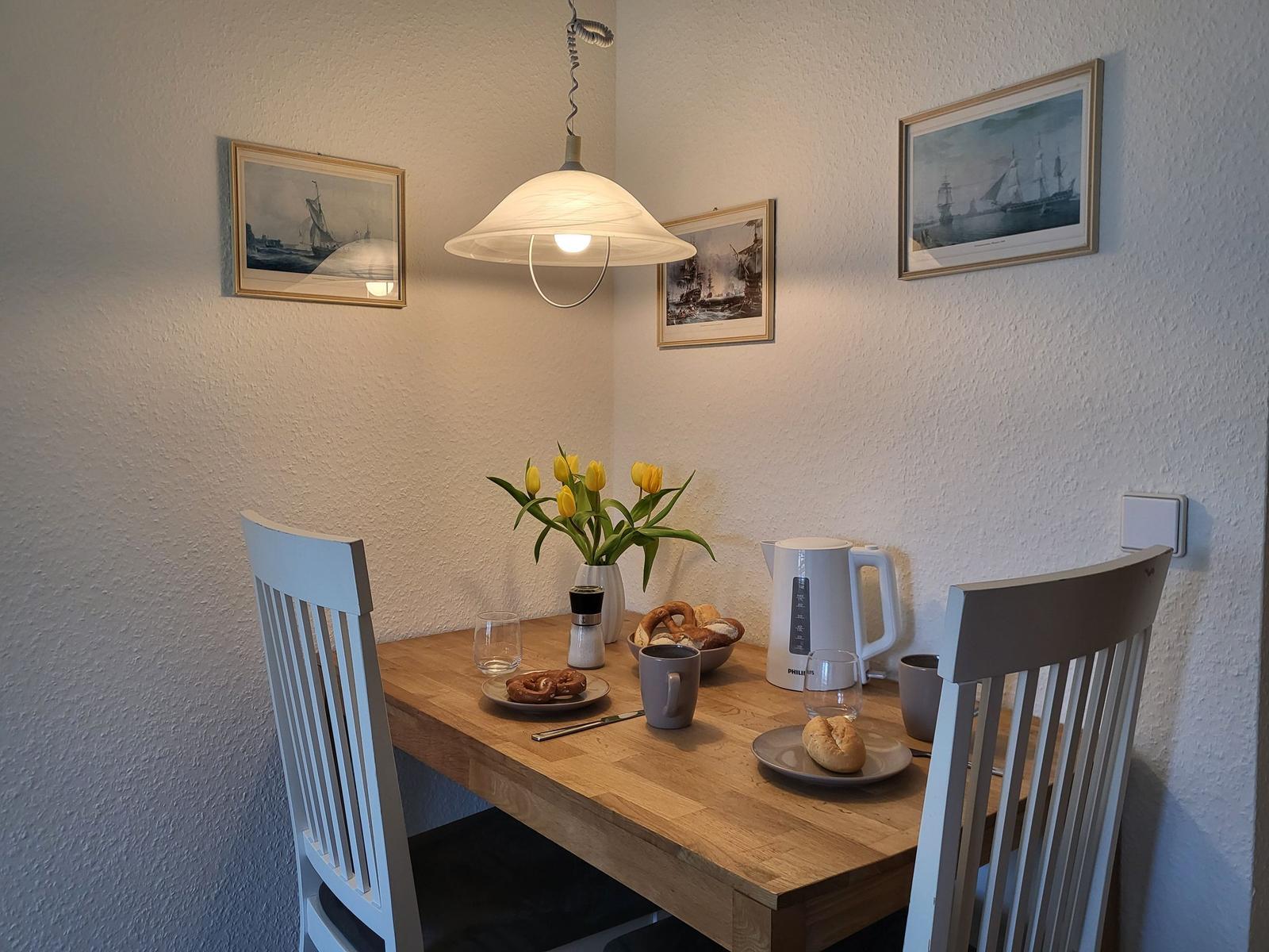 Esstisch mit zwei Stühlen, Blumen, Kaffee und Gebäck.