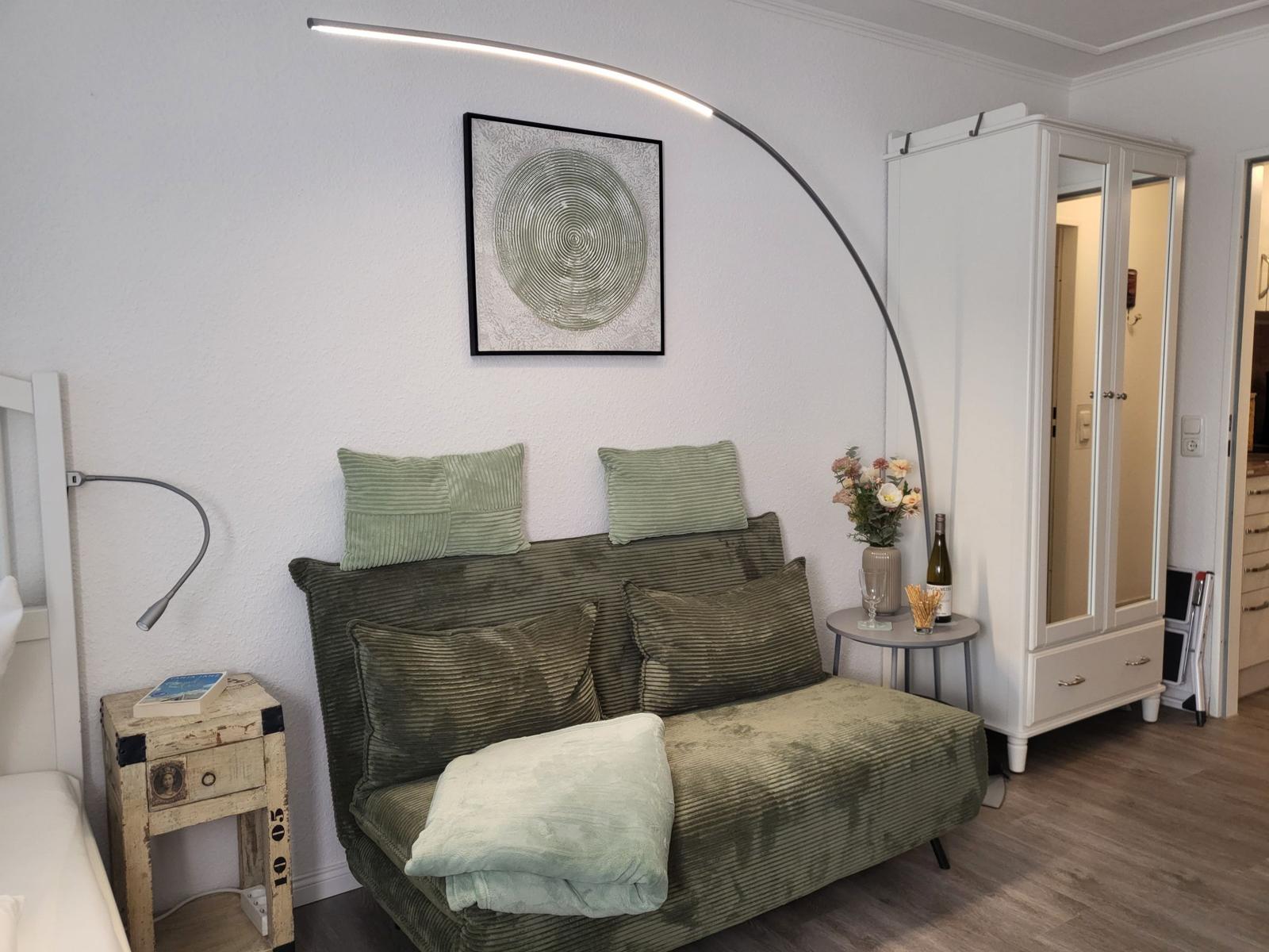 Ein Sofa mit Kissen, eine Stehlampe und ein Schrank sind sichtbar.